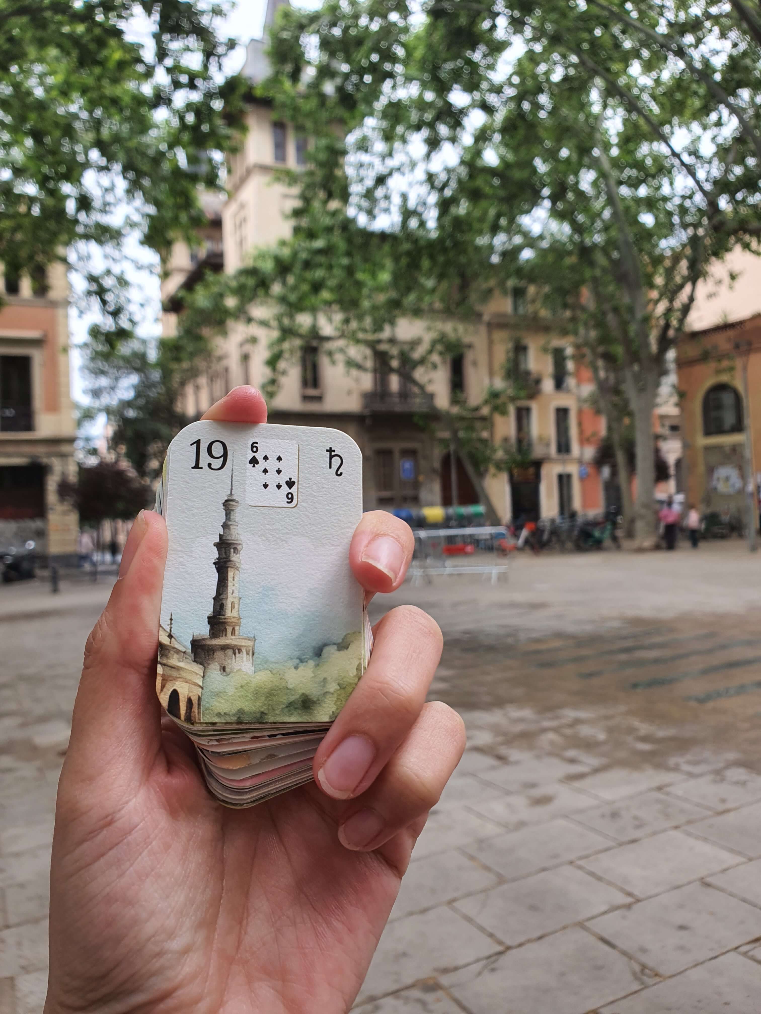 Mini mazo acuarela Petit Lenormand sostenido en la mano frente a una plaza arbolada