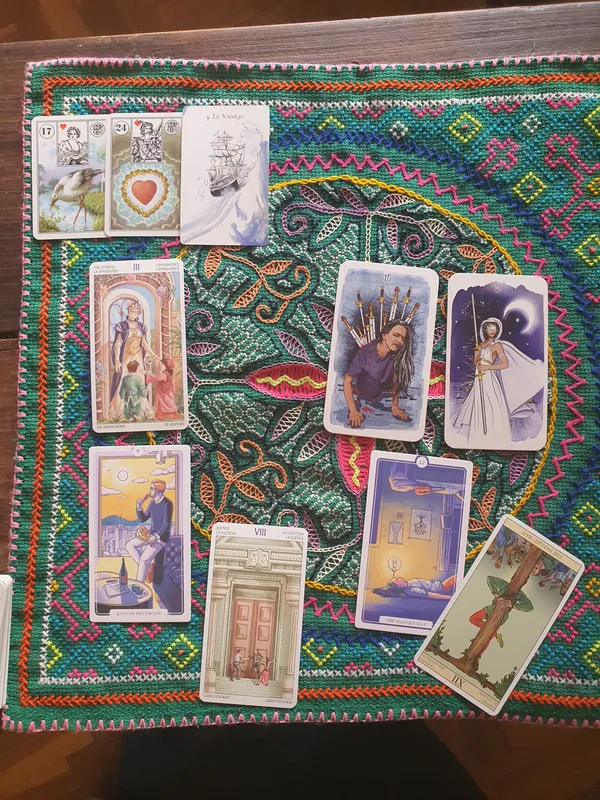 Three Lenormand cards above several tarot styles on an embroidered mat.