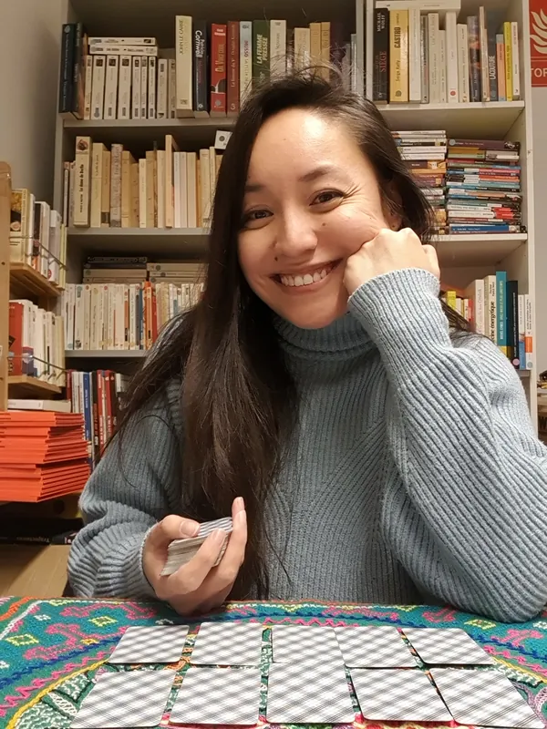 Isabelle smiling in front of her bookshelves, holding a deck, with face-down cards in front of her.