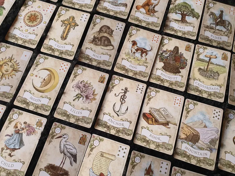 Vue rapprochée de cartes Old Style Lenormand sur un tissu sombre, dont le Chien, le Bouquet, la Lune et le Livre.