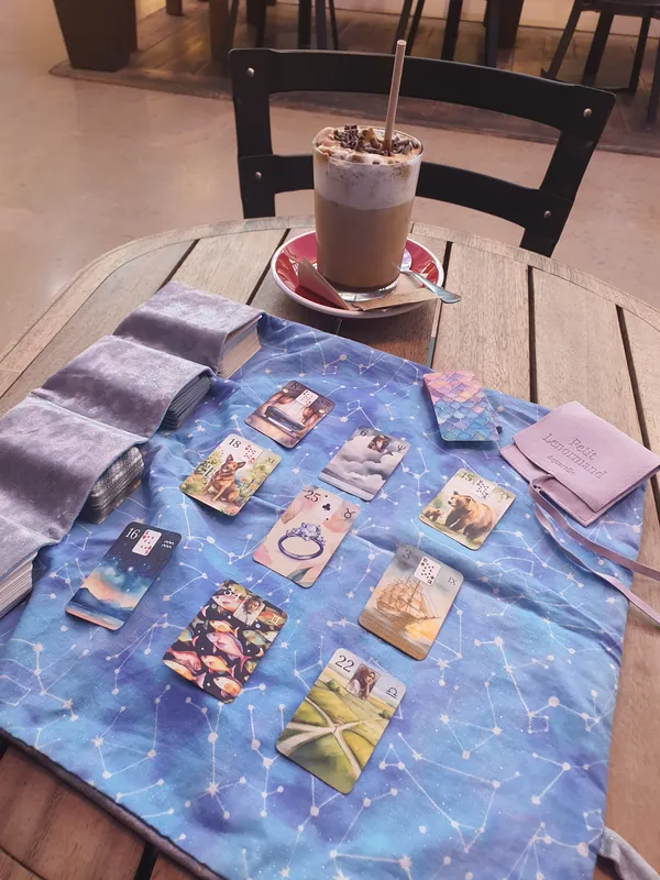 Nine Aquarelle cards on a blue star-patterned cloth, with a cup and several pouches on a wooden table.
